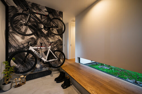 自転車を壁掛けにした玄関。地窓の緑が白黒の空間に映える。